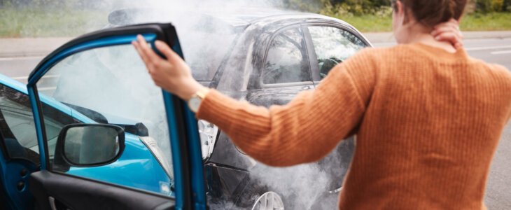 Rear View Of Female Motorist With Head Injury Getting Out Of Car After Crash