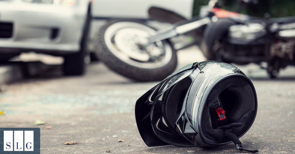 Motorcycle helmet at a crash scene with a fallen motorcycle and damaged vehicles in the background.